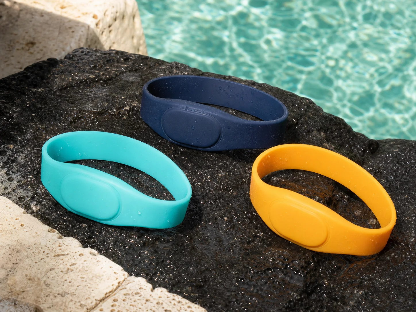 Three unbranded silicone RFID wristbands on volcanic stone beside a pool